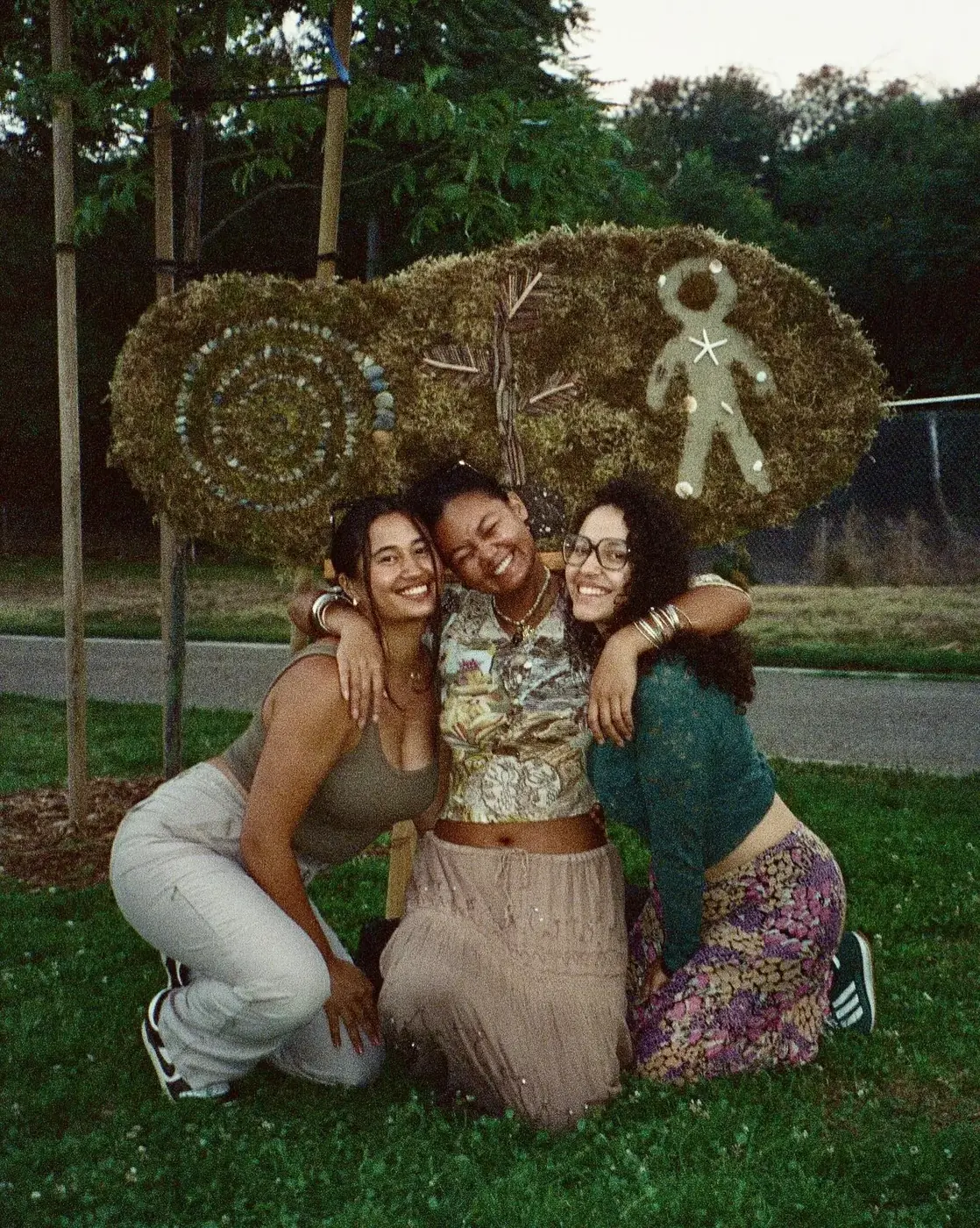 Three friends seated together in front of a woven flower installation