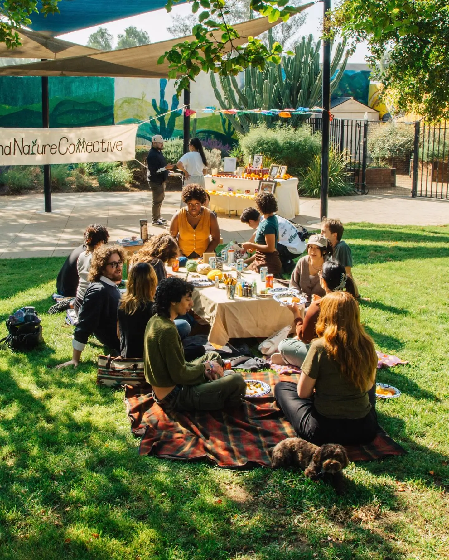 Community members sharing food and conversation on blankets under the trees